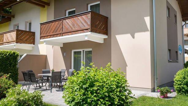 Een gebouw met twee verdiepingen, een balkon, een terras en een keurig onderhouden tuin.