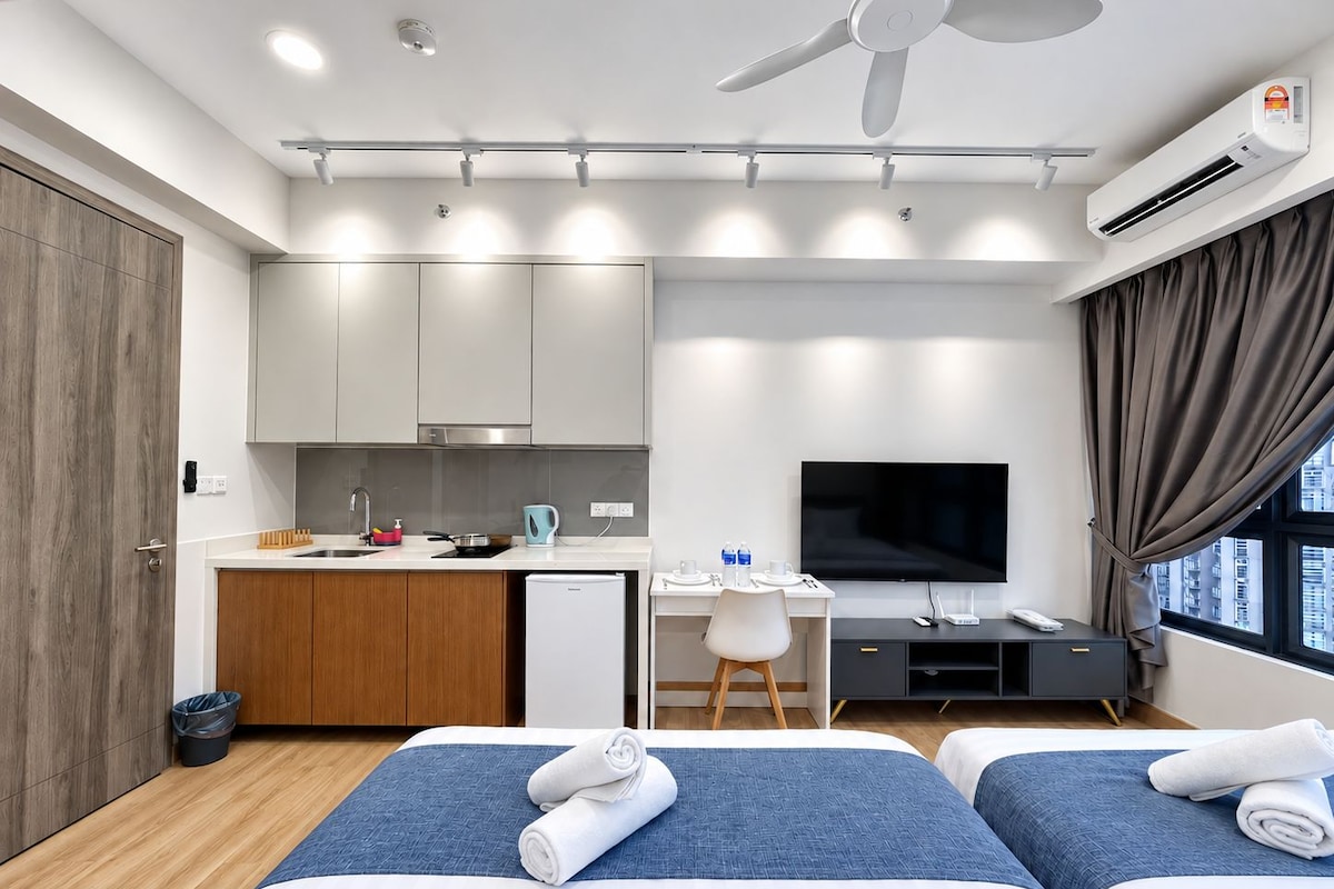 A modern hotel room with a kitchenette, a flat-screen TV, a desk, and two beds.