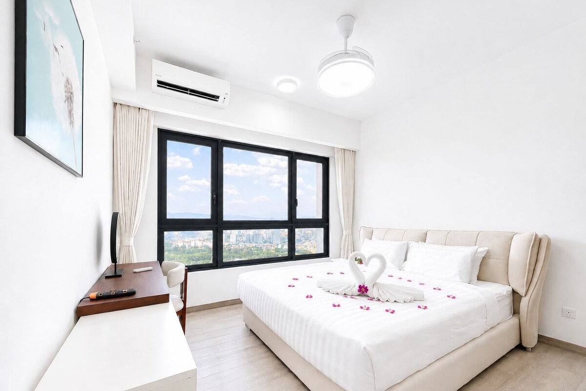 A hotel room with a large bed, a desk, an air conditioning unit, and a view of the city through a large window.