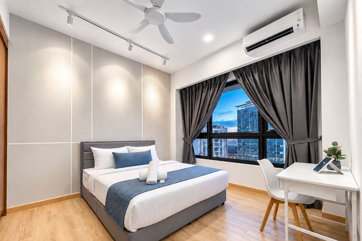 A modern hotel room with a bed, a desk, and a view of the cityscape through large windows.
