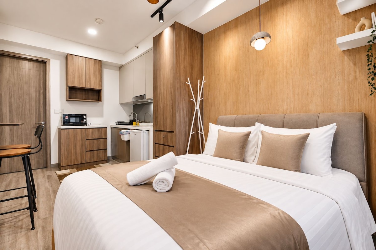A hotel room with a bed, a desk, a kitchenette, and a wooden accent wall.