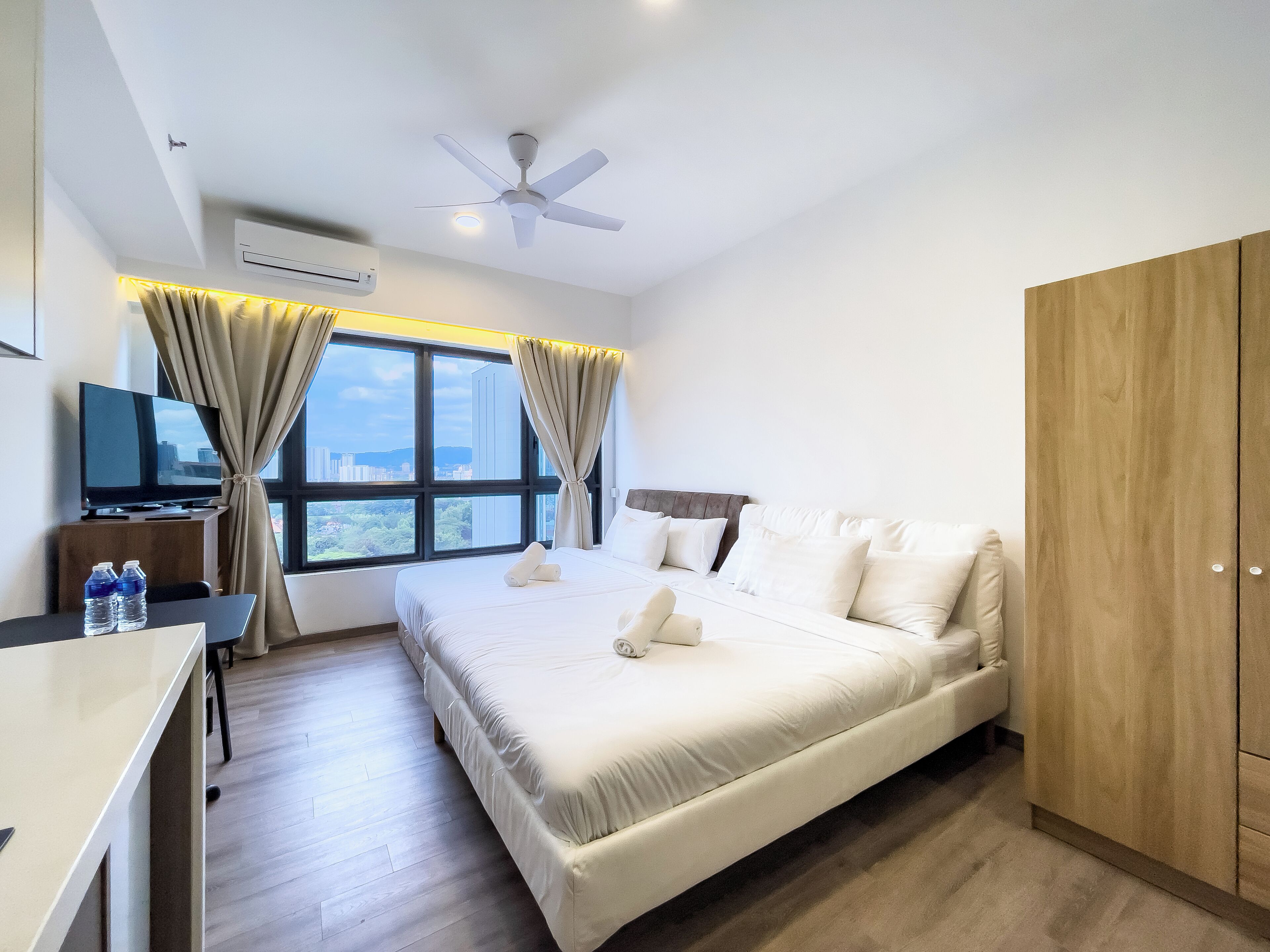 A hotel room with a bed, a desk with a TV, a wardrobe, and a window with curtains.