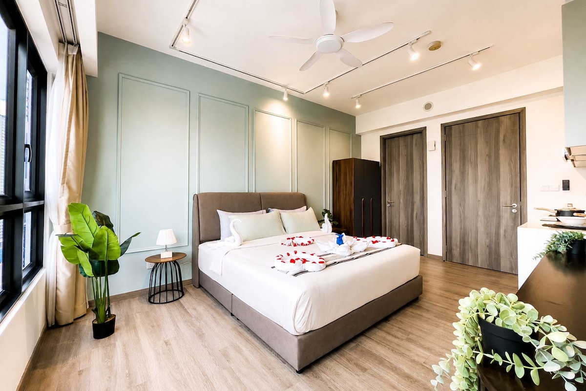 A modern hotel room with a large bed, a ceiling fan, a small side table, and a potted plant.