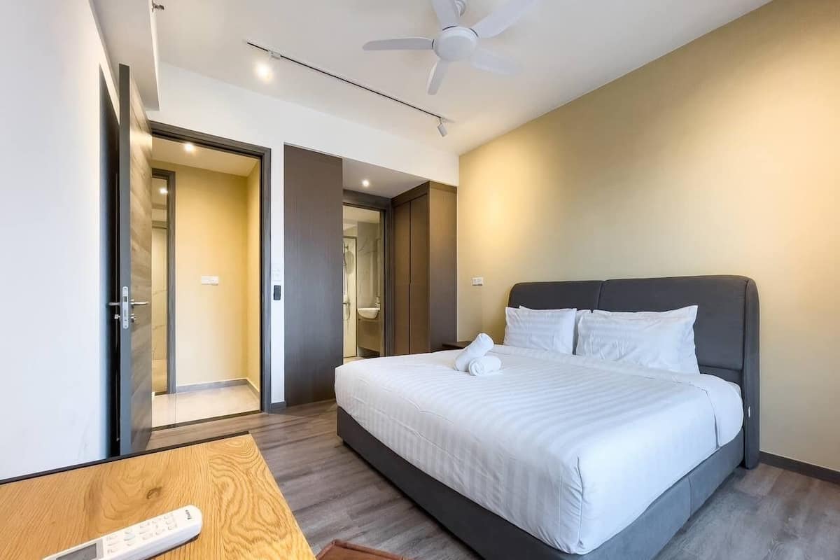 A modern hotel room with a large bed, a wooden side table, and a ceiling fan.