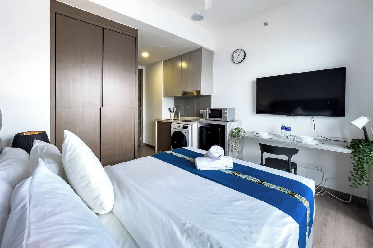 A hotel room with a bed, a desk with a computer, a microwave, and a TV.
