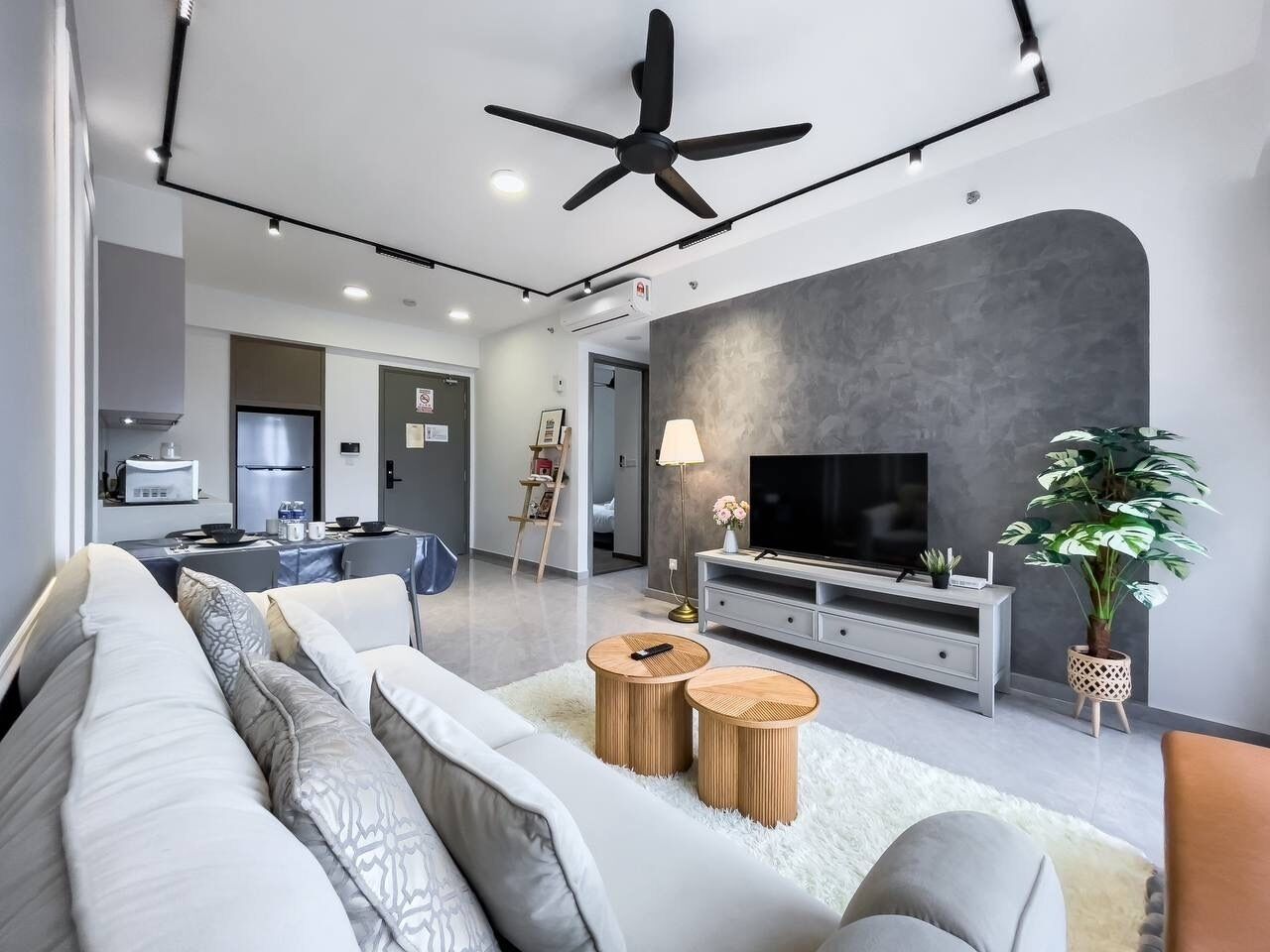 A modern living room with a sofa, two round wooden side tables, a flat-screen TV, a ceiling fan, and a grey accent wall.