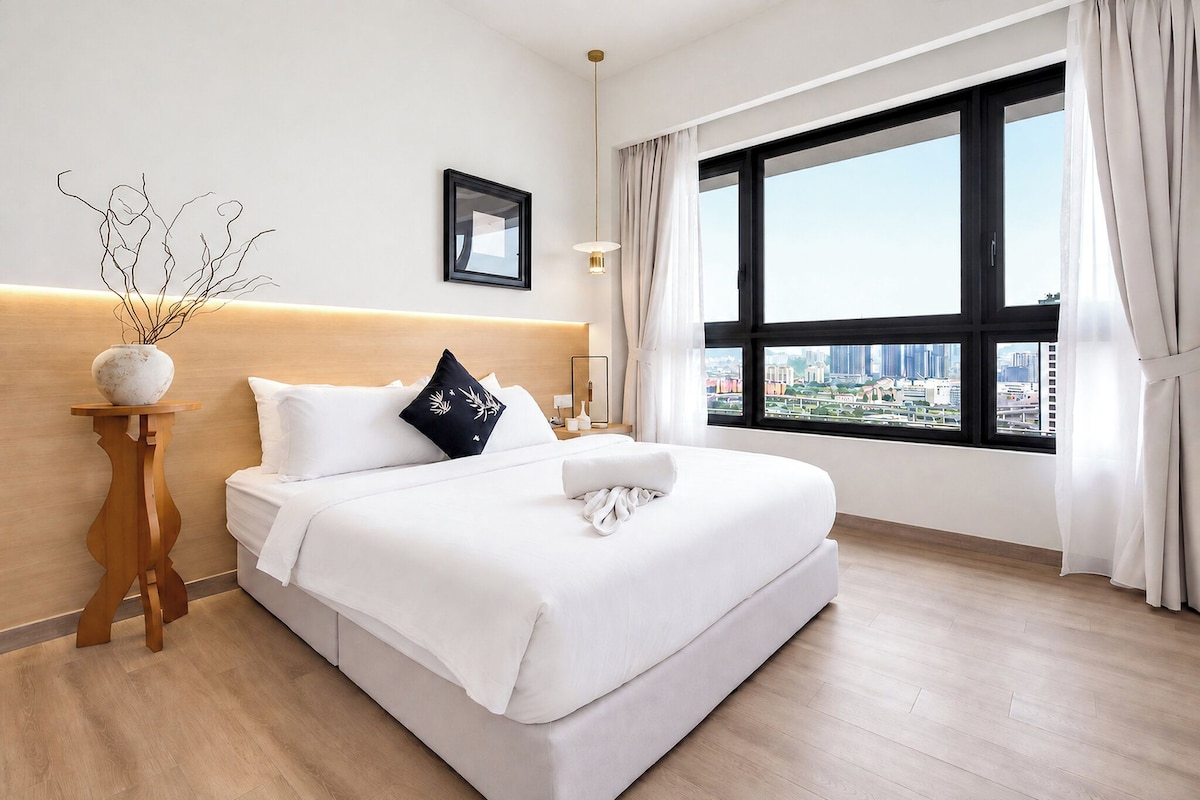 A modern hotel room with a large bed, a bedside table with a vase, and a city view through the window.