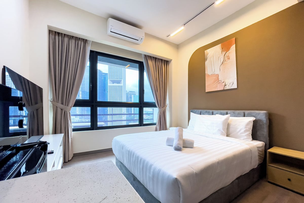A hotel room with a bed, a desk, a TV, and a window with curtains.