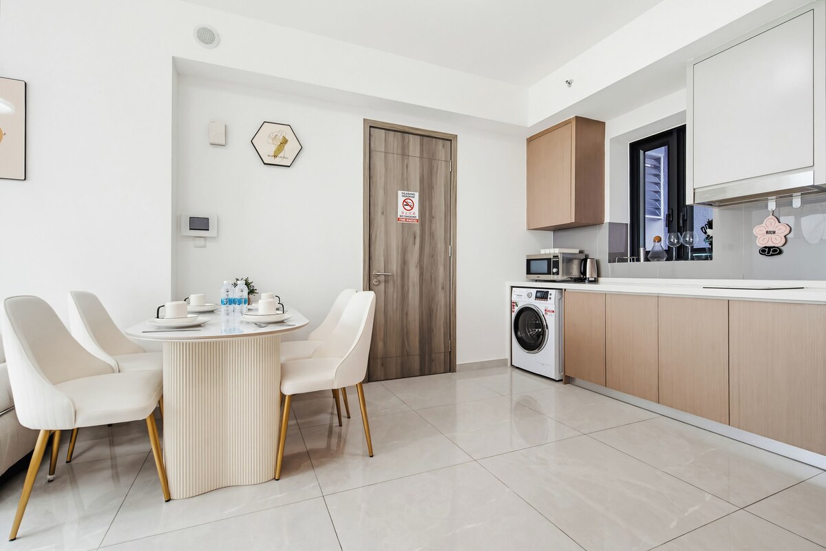 Een moderne keuken met een ingebouwde wasmachine, een eethoek met een ronde tafel en stoelen, en een houten deur met een 'Niet roken'-bordje.