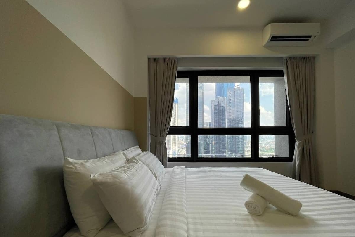 A hotel room with a large bed, a headboard, a window with curtains, and a city view.