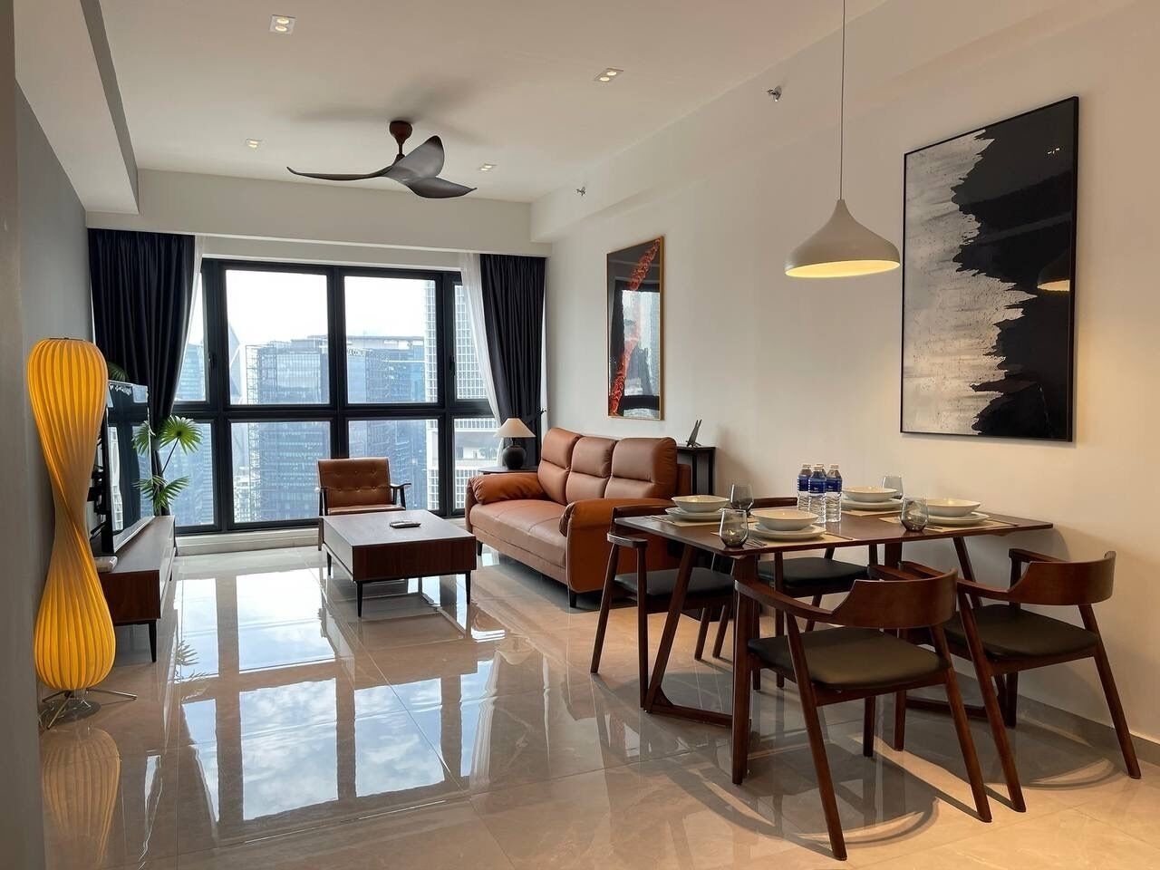 A modern living room with a sofa, dining table, and chairs, large windows with curtains, and a city view.