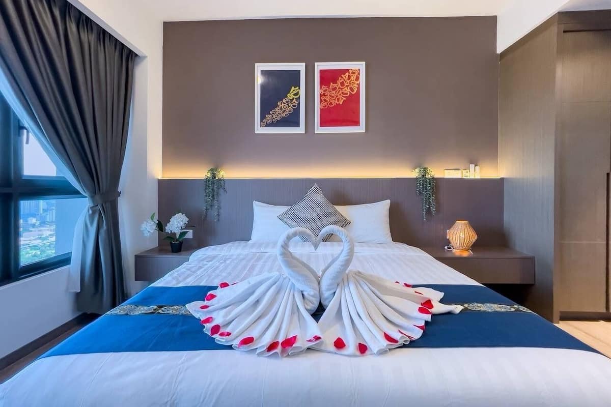 A hotel room with a bed featuring a swan-shaped towel arrangement, a city view, and two framed artworks on the wall.