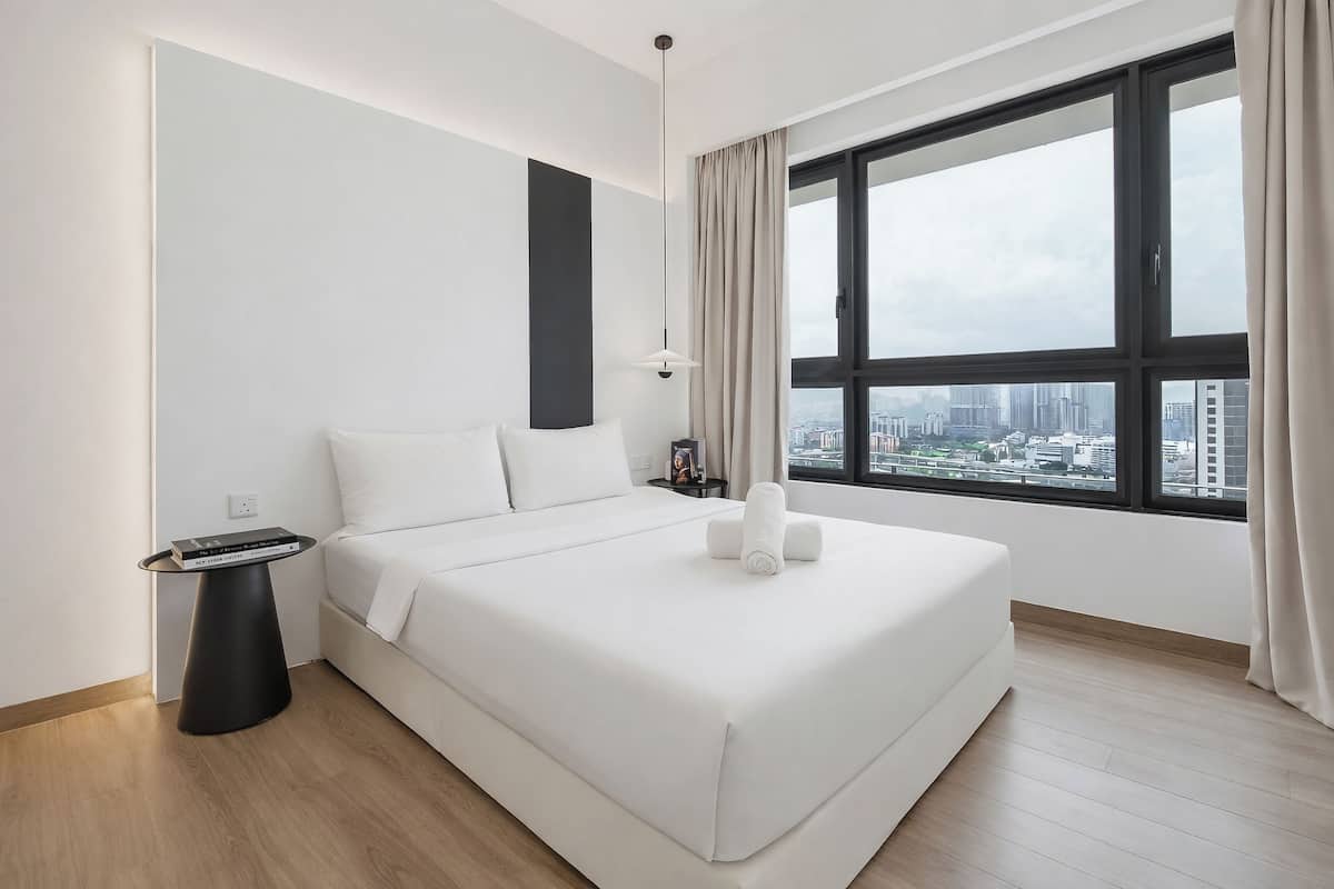 A modern hotel room with a large bed, a bedside table, a nightstand, a window with a city view, and a cityscape visible through the window.