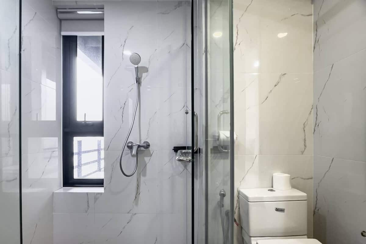 A modern bathroom with a glass-enclosed shower, a toilet, and a window.