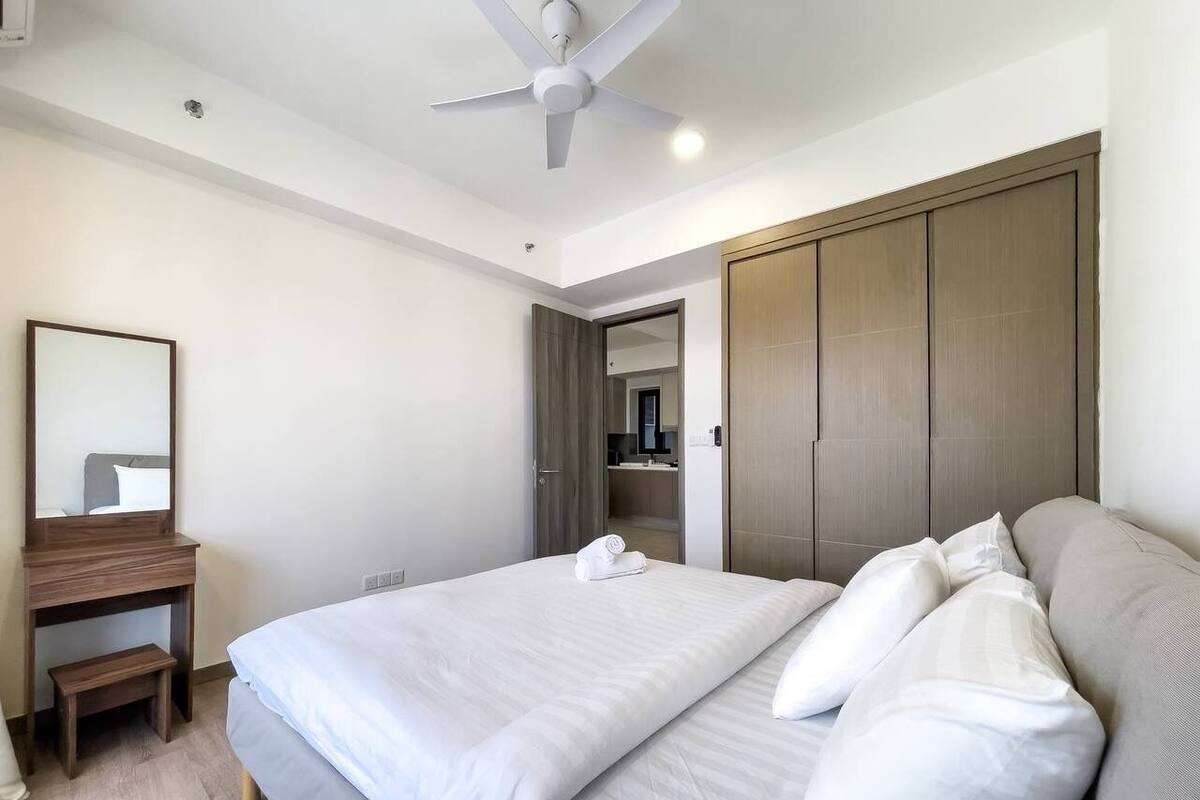 A hotel room with a bed, a desk, a mirror, a wardrobe, and a ceiling fan.