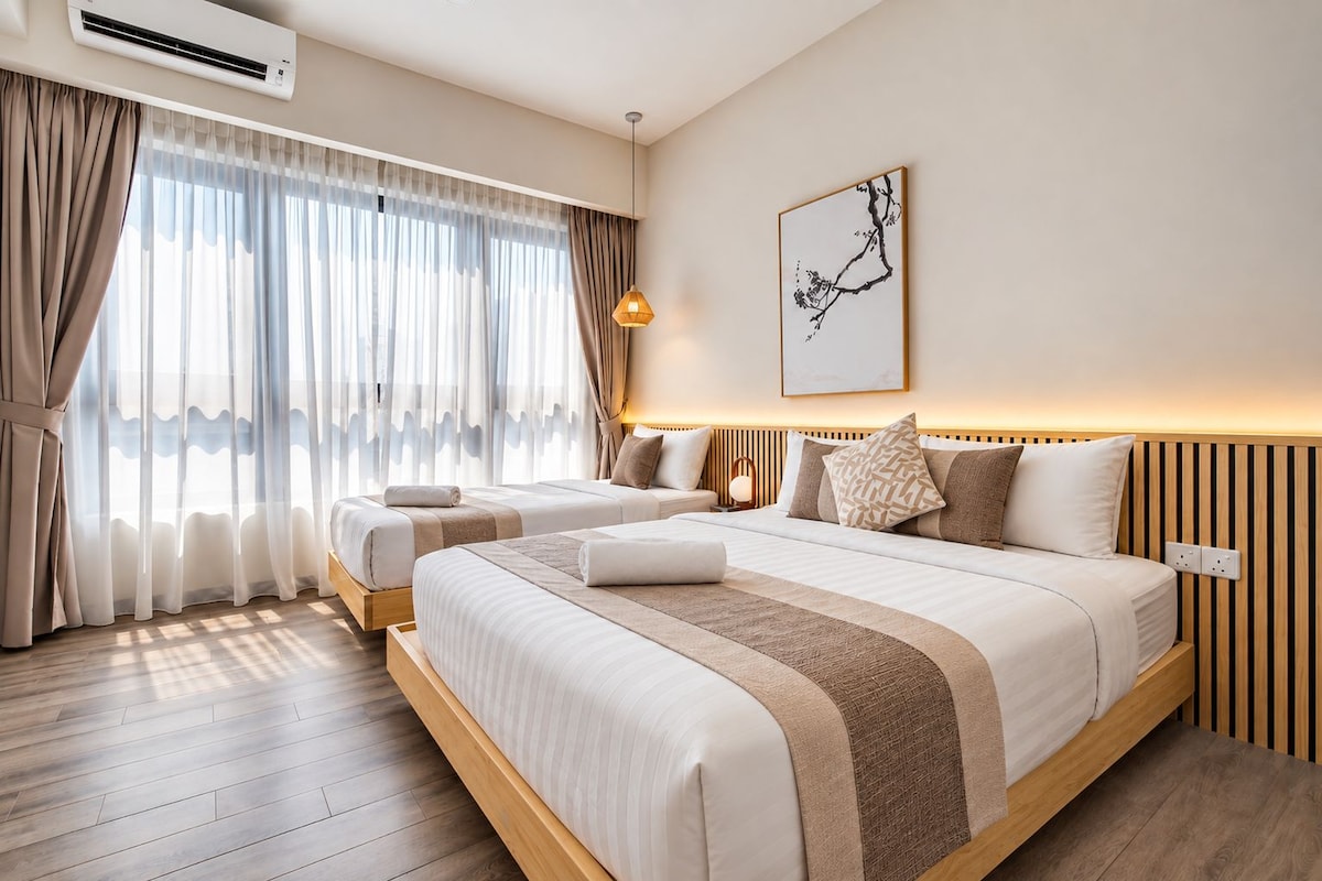 A hotel room with two beds, a large window with sheer curtains, a wall-mounted air conditioner, and a framed artwork.