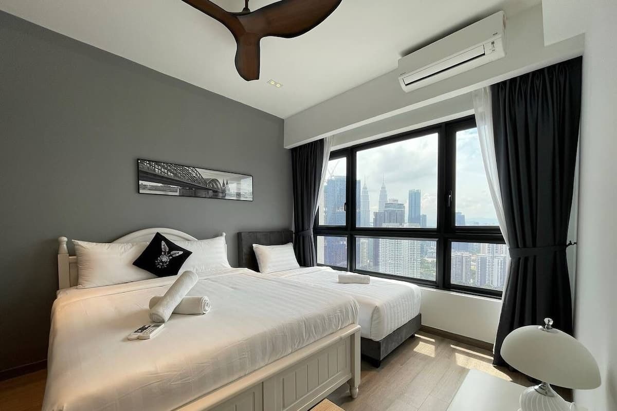 A modern hotel room with two beds, a city view, a ceiling fan, and a desk with a lamp.