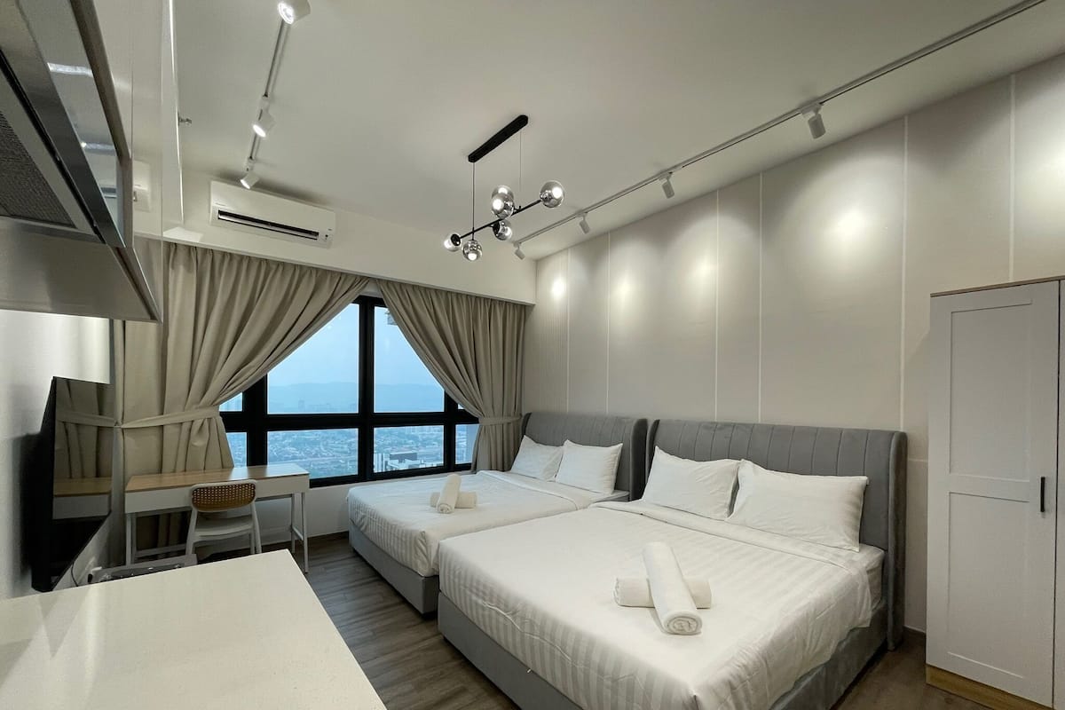 A modern hotel room with two beds, a desk, and a view of the city.