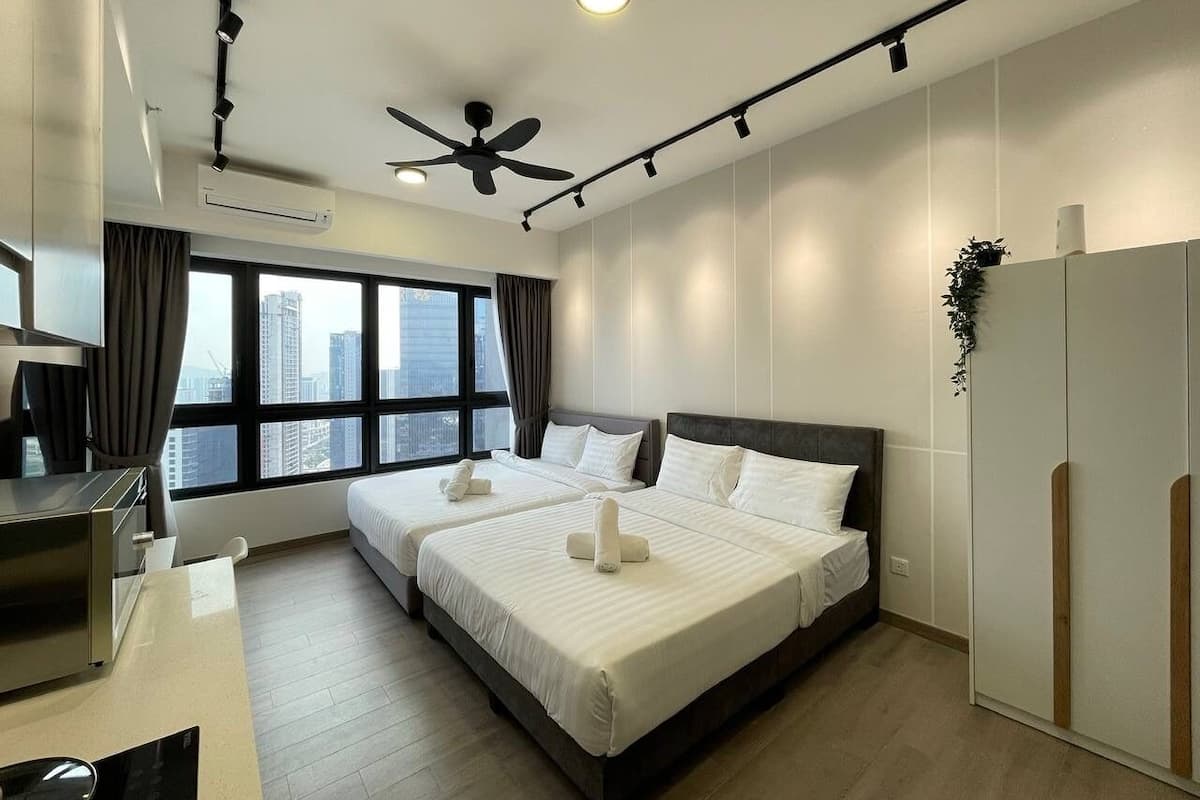 A modern hotel room with two beds, a desk, a ceiling fan, and a large window with a city view.