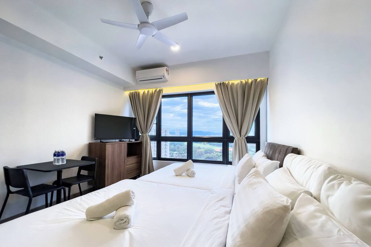 A hotel room with a bed, a desk with a chair, a television, and a window with curtains.