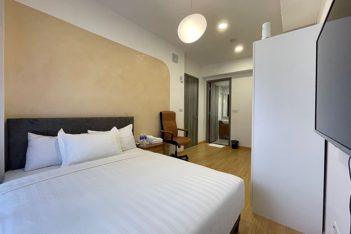 A hotel room with a large bed, a chair, a television, and a bathroom visible through an open door.