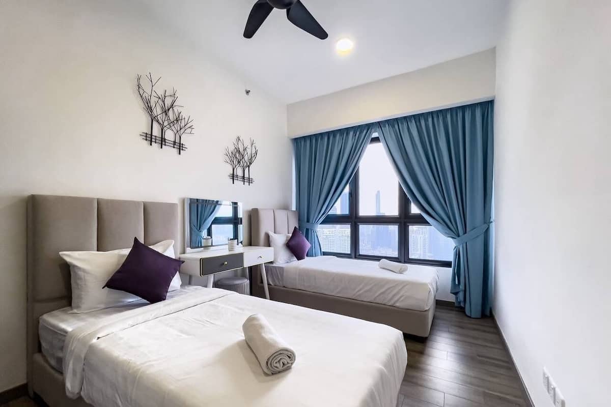 A hotel room with two beds, a desk, and a large window with curtains.