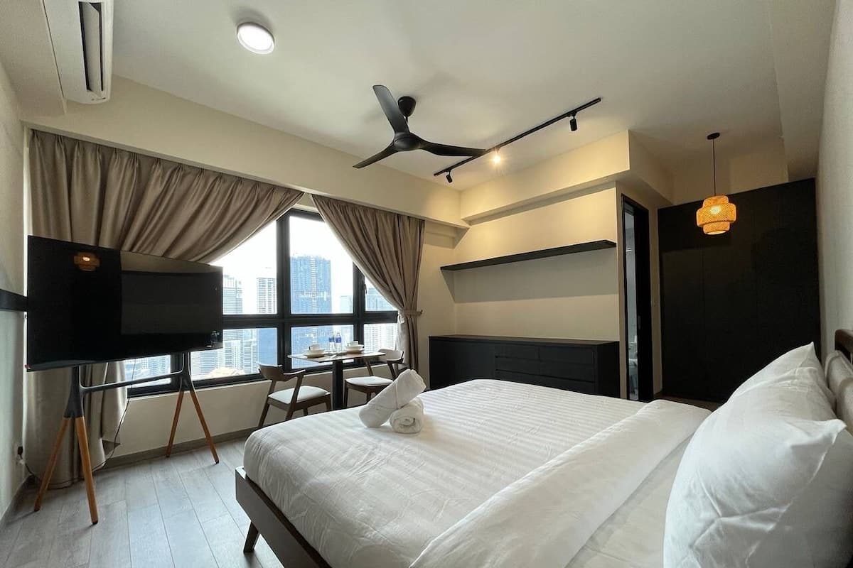 A modern hotel room with a large bed, a desk, a flat-screen TV, and a city view.