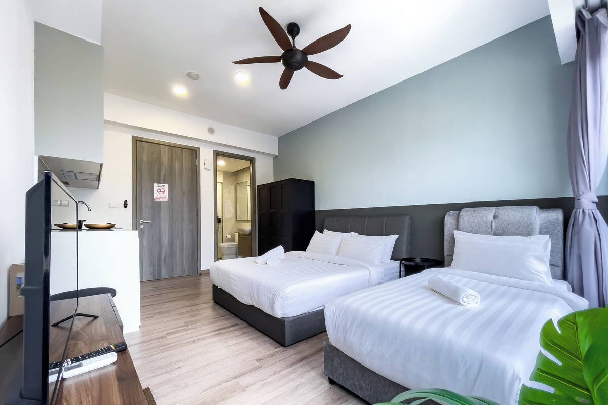 A hotel room with two beds, a ceiling fan, a TV, and a bathroom visible through an open door.
