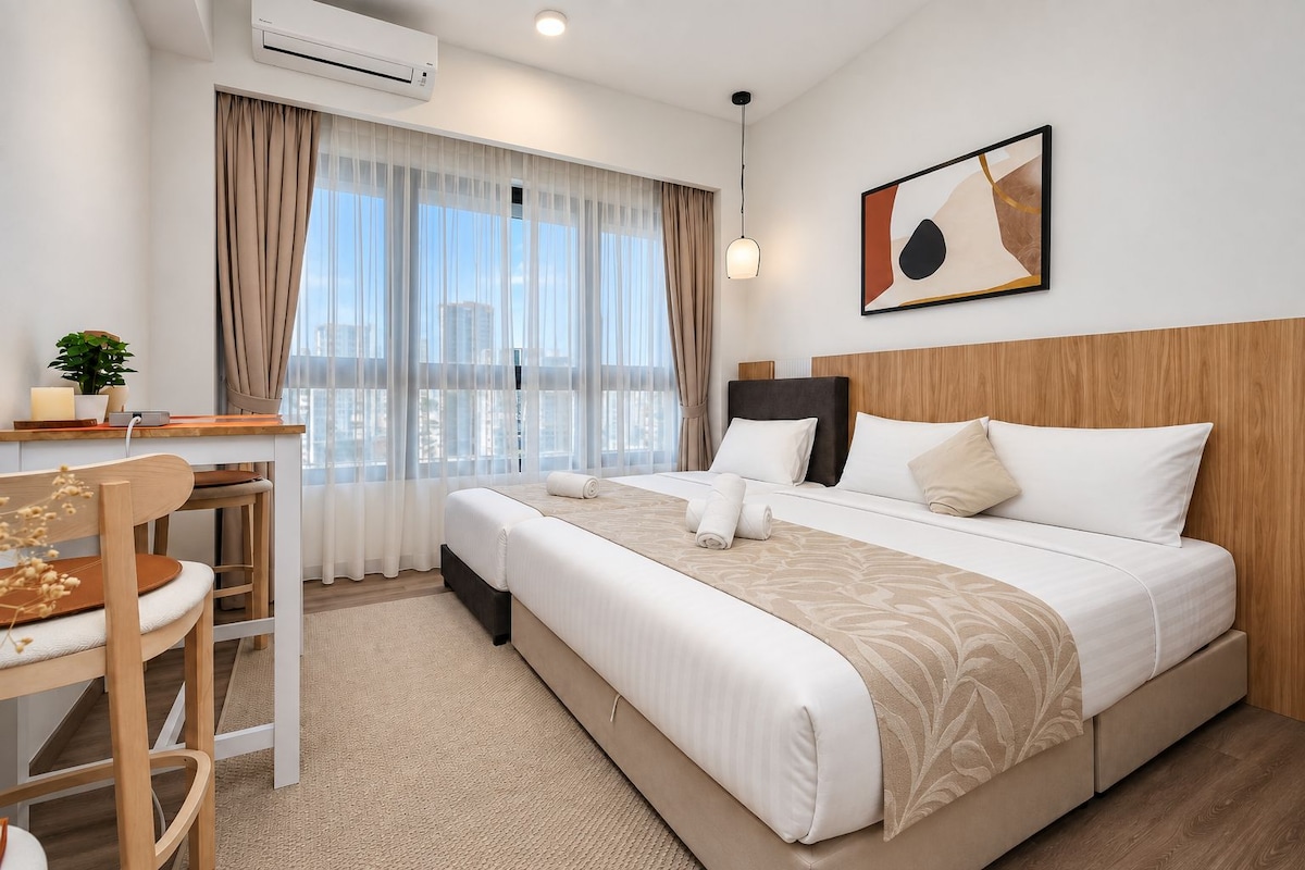 A hotel room with a bed, a desk, a chair, a potted plant, and a city view.
