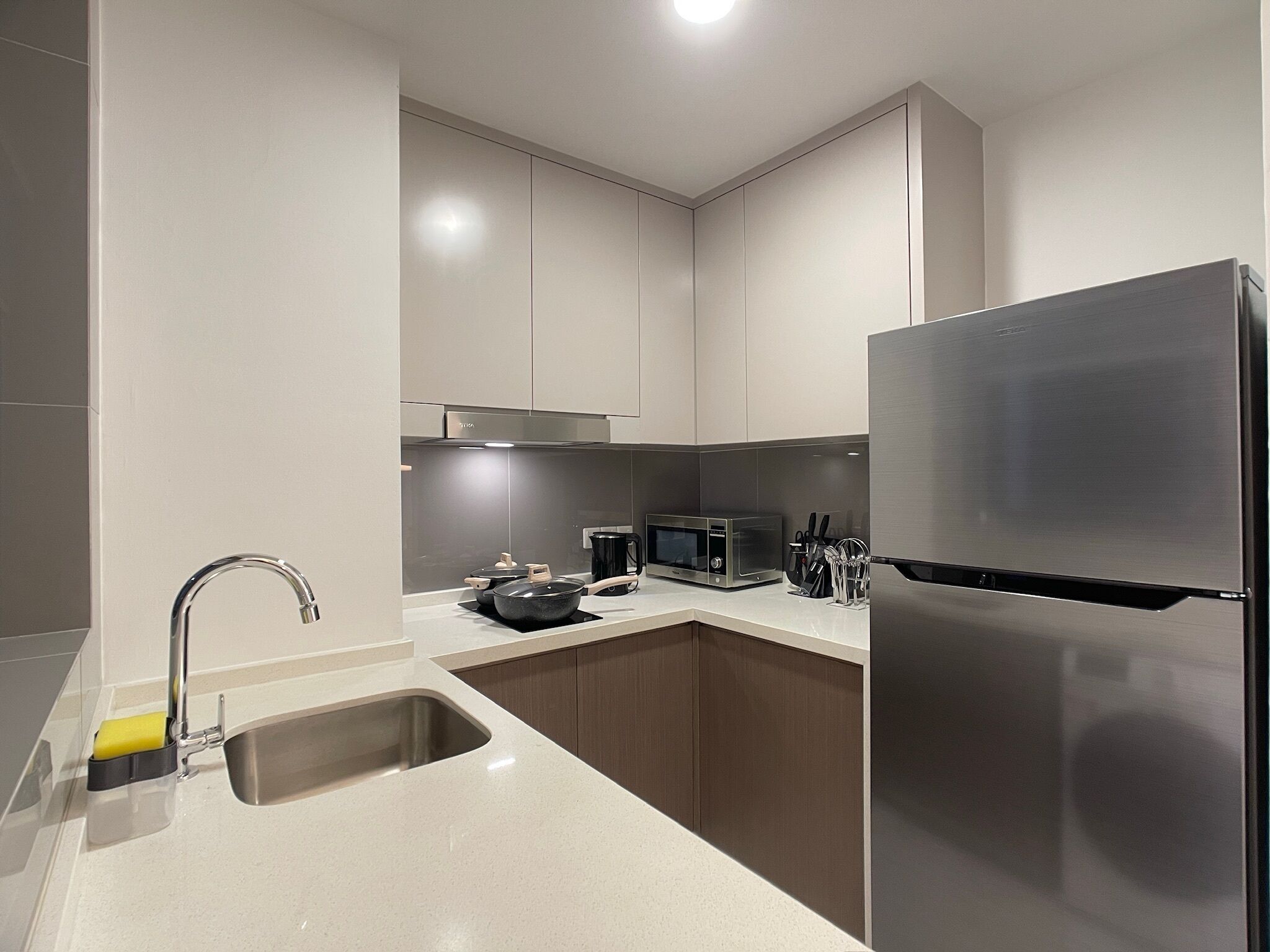 Eine moderne Küche mit einem Edelstahl-Kühlschrank, einer Mikrowelle und einem Waschbecken mit Armatur.