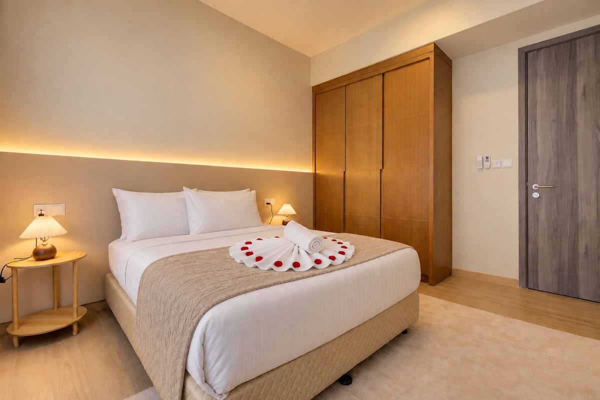 A hotel room with a large bed, bedside lamps, a wooden wardrobe, and a door with a handle.