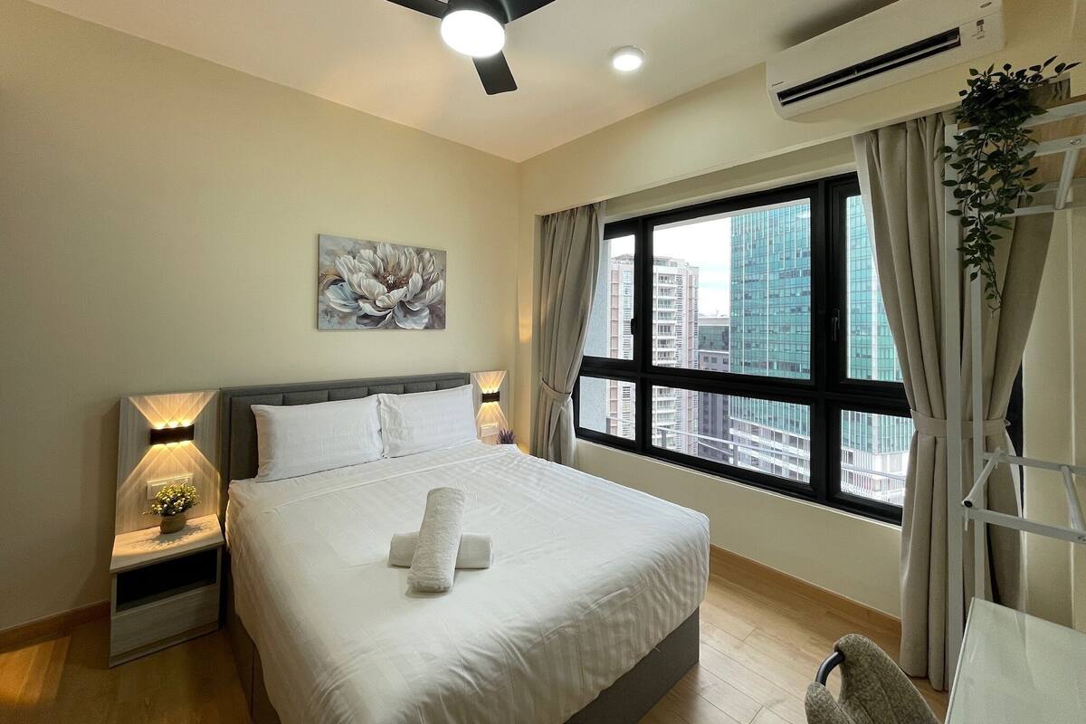 A hotel room with a bed, nightstands, a ceiling fan, an air conditioner, a window with curtains, and a city view.