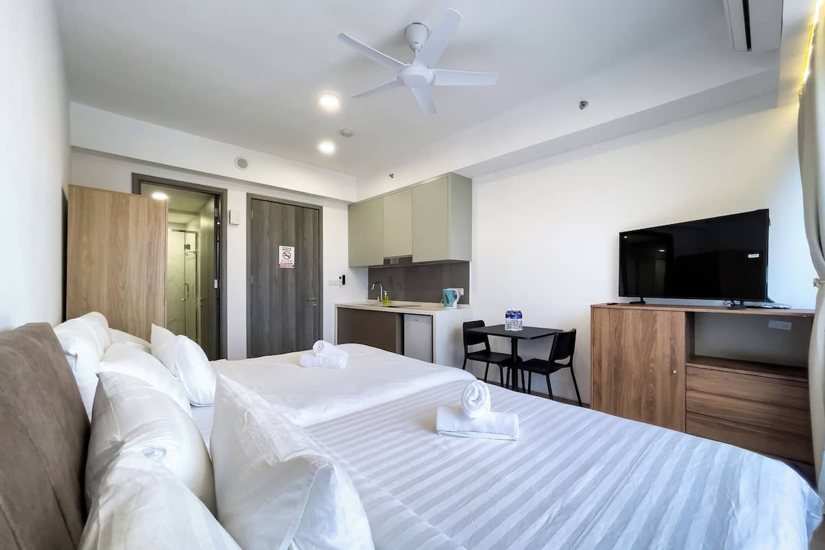 A hotel room with two beds, a TV, a desk, and a kitchenette.