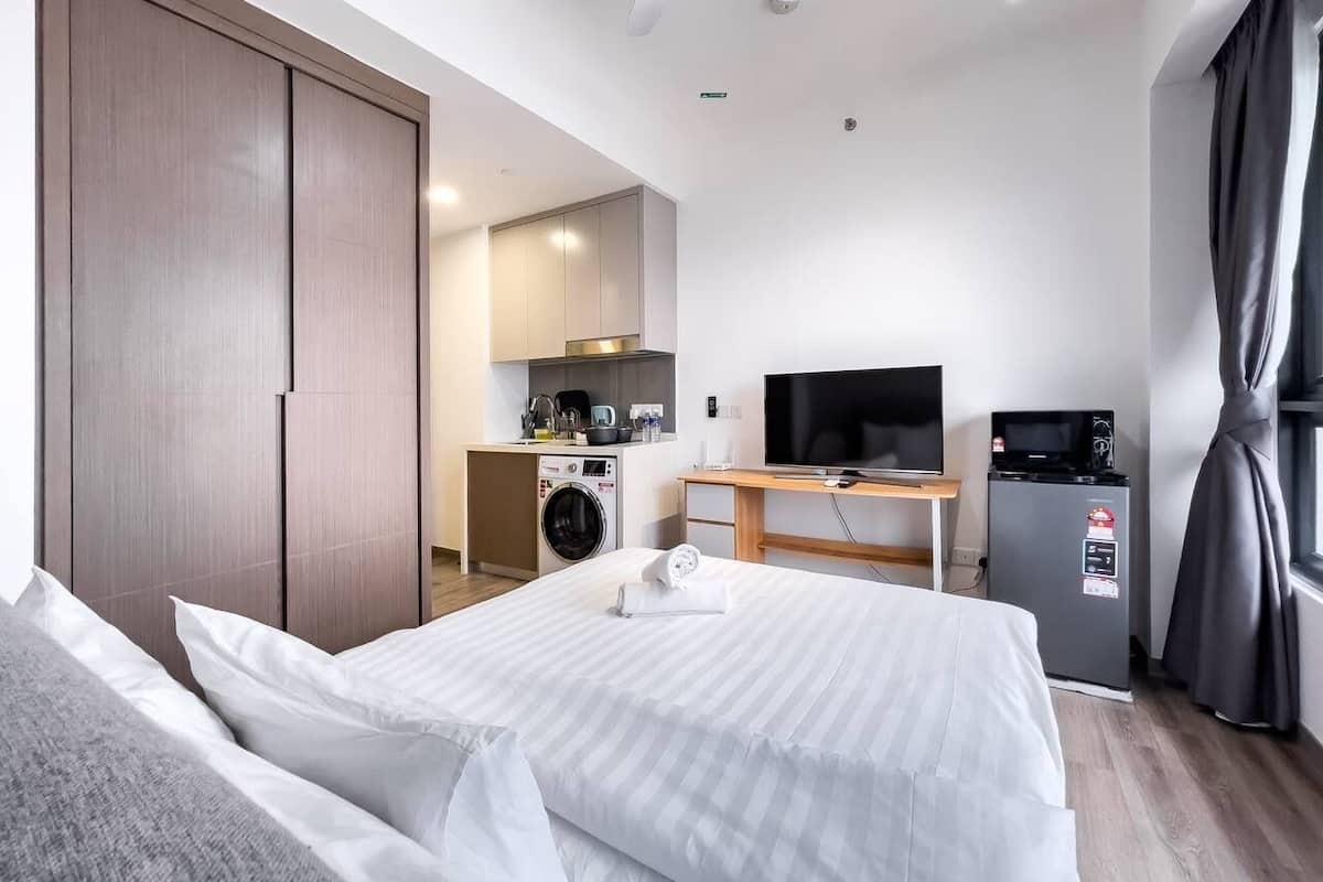 A hotel room with a bed, a TV, a mini-fridge, a washing machine, and a kitchenette.