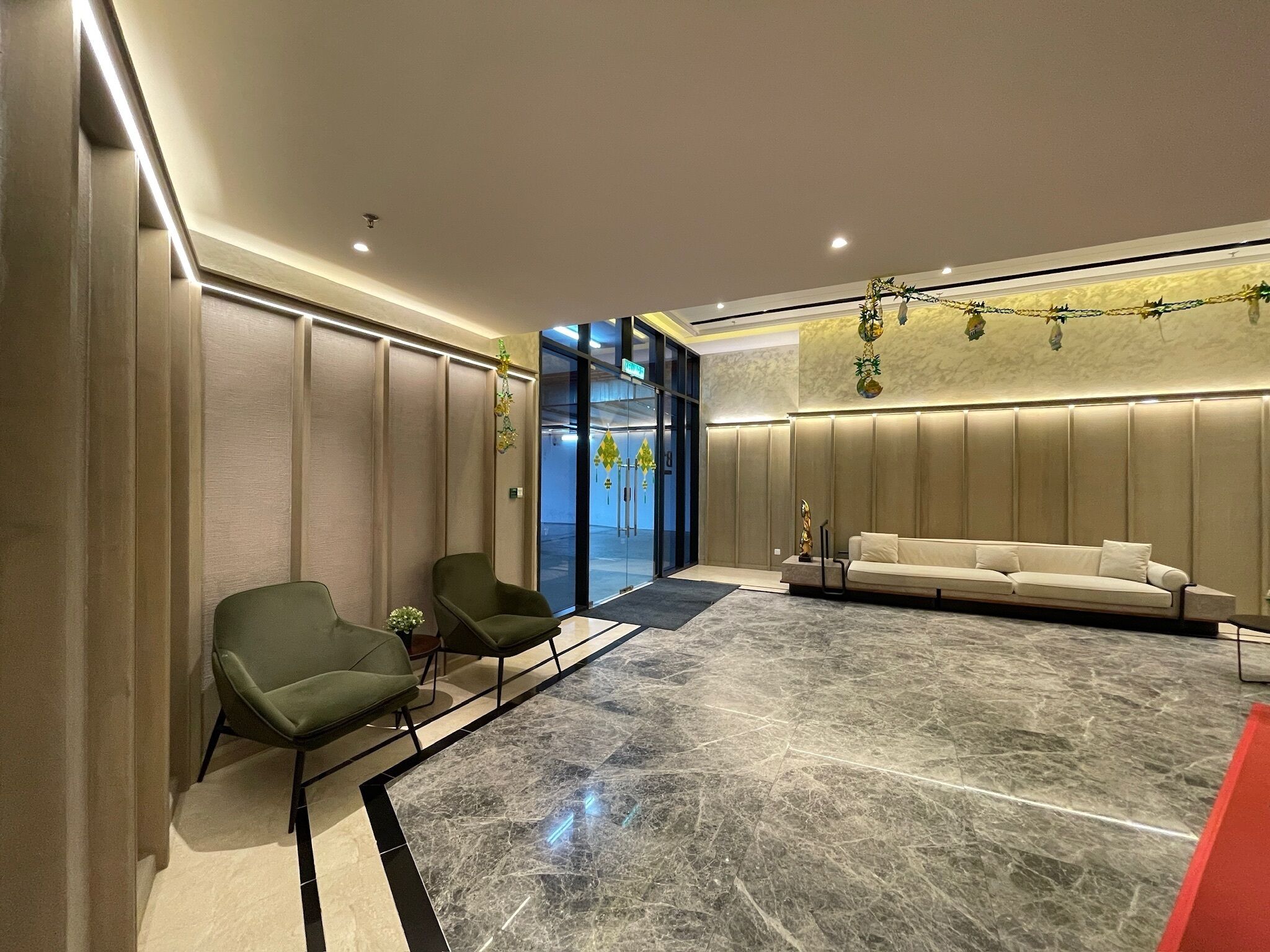 Un hall d’entrée moderne avec un sol en marbre, des fauteuils verts, un canapé blanc et une entrée en verre.