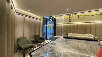 A modern lobby with a marble floor, green chairs, a white sofa, and a glass entrance.
