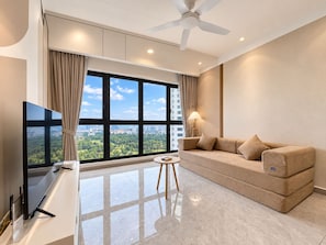 A modern living room with a flat-screen TV, a sofa, a lamp, and a view of a cityscape through large windows.