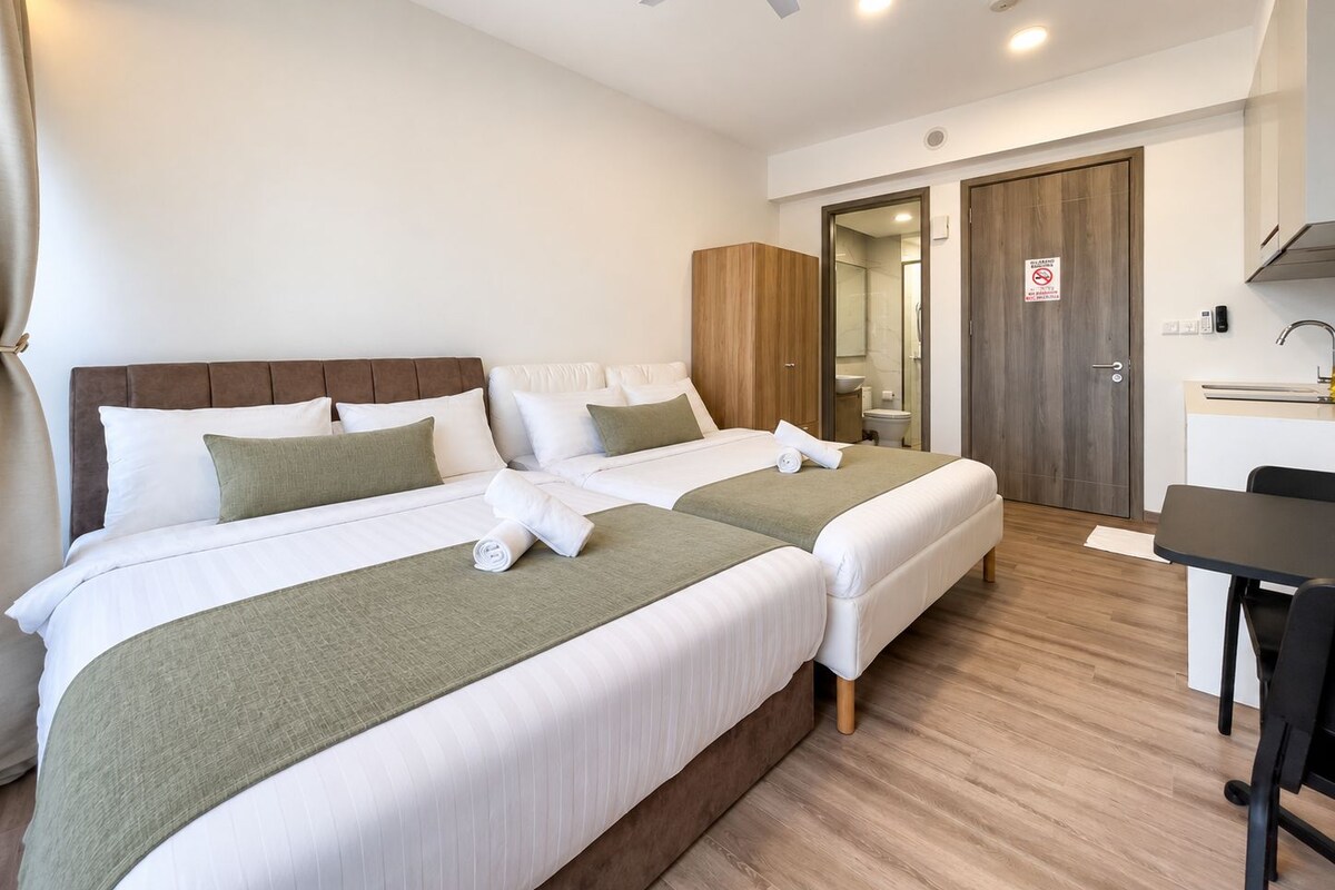 Een hotelkamer met twee bedden, een bureau, een stoel, een plafondventilator en een badkamedeur.