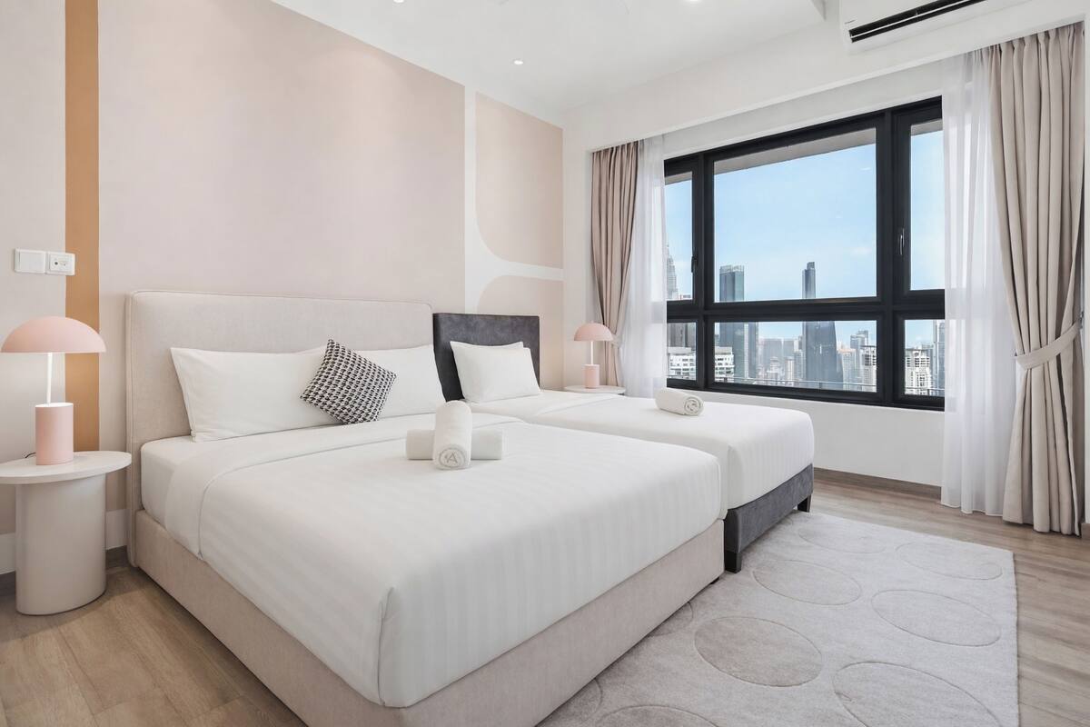 A modern hotel room with two beds, a large window with a city view, and a minimalist design.