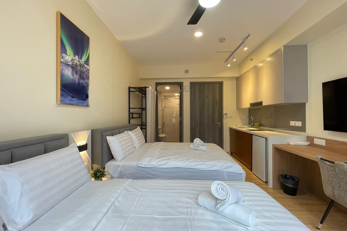 A hotel room with two beds, a desk, a TV, and a bathroom visible through an open door.