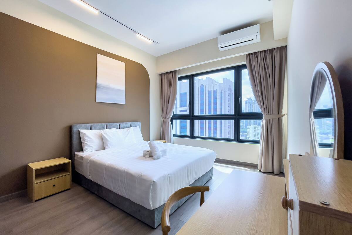 A modern hotel room with a large bed, a wooden nightstand, a desk, and a view of the cityscape through the window.