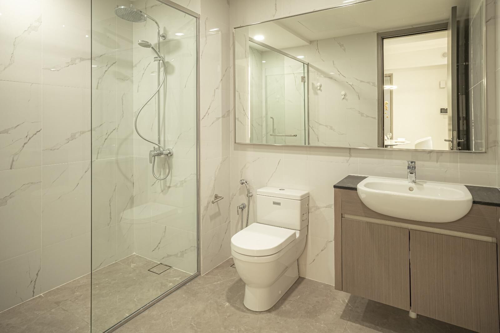 Een moderne badkamer met een douchecabine van glas, een toilet en een wastafel met spiegel erboven.