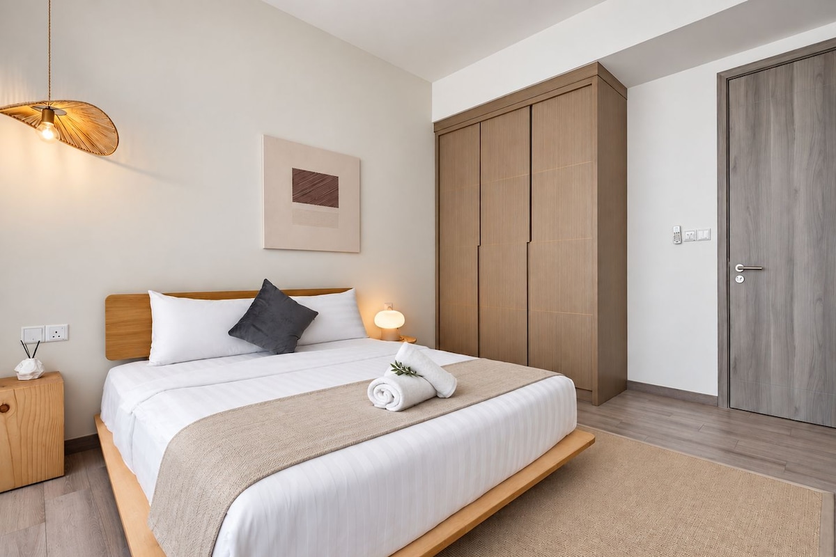 A hotel room with a bed, bedside table, lamp, wardrobe, and a framed picture on the wall.