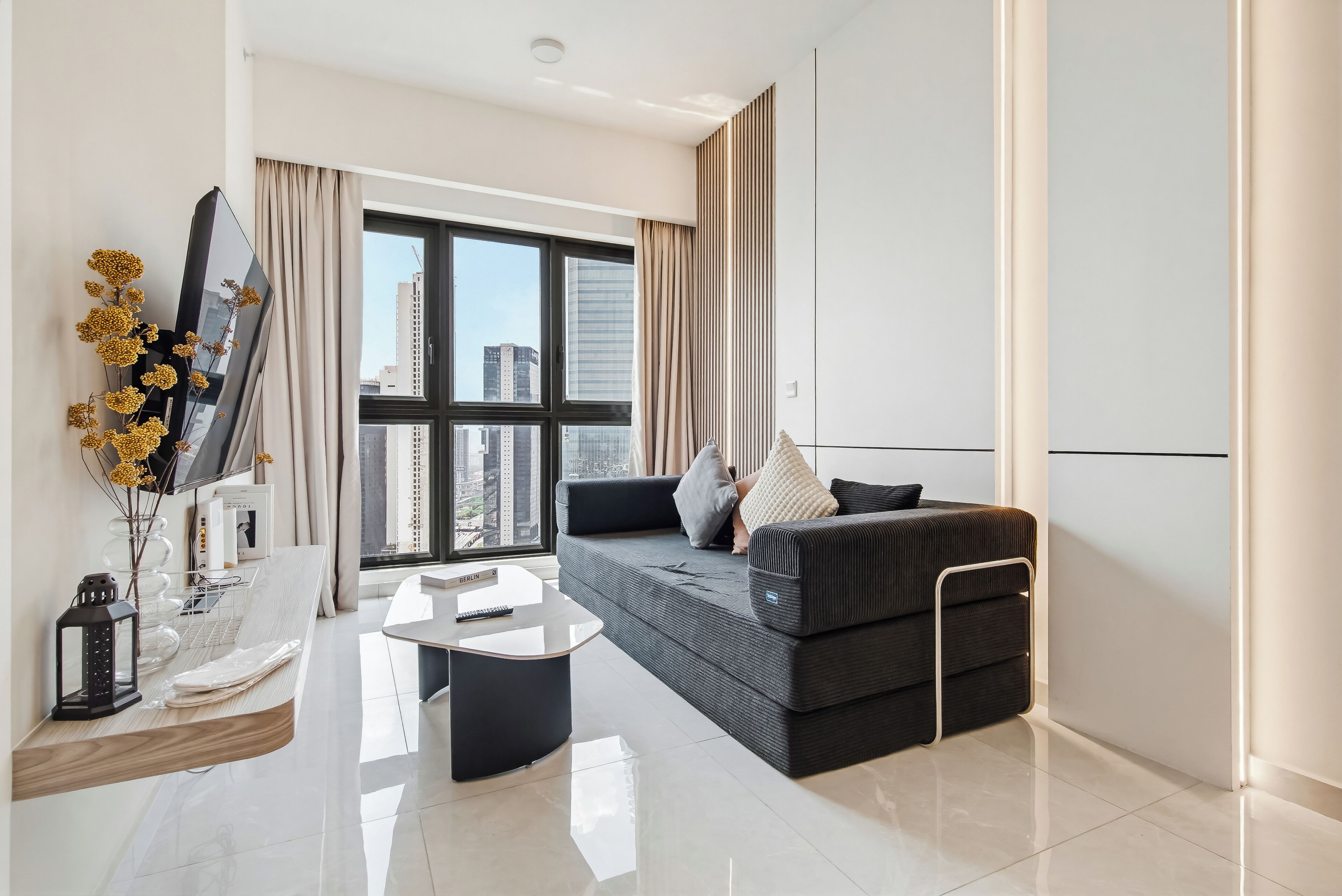 A modern living room with a sofa, a coffee table, a TV, and a large window with curtains.