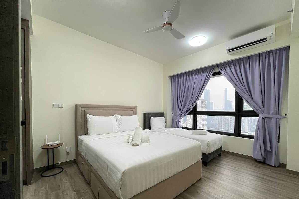 A hotel room with a bed, a bedside table, a window with curtains, an air conditioning unit, and a ceiling fan.