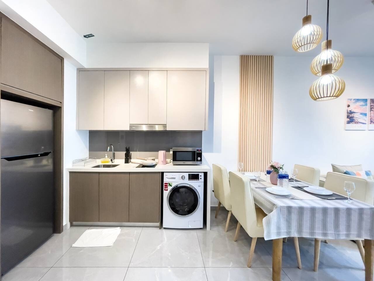 A modern kitchen with a built-in washing machine, a dining area with a table set for two, and a large window with vertical blinds.
