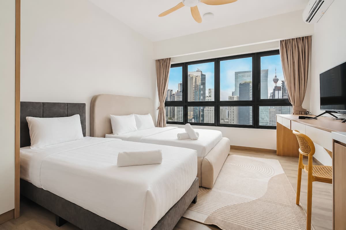 Hotelkamer met twee bedden, een bureau, een stoel, een groot raam met stadszicht en een plafondventilator.