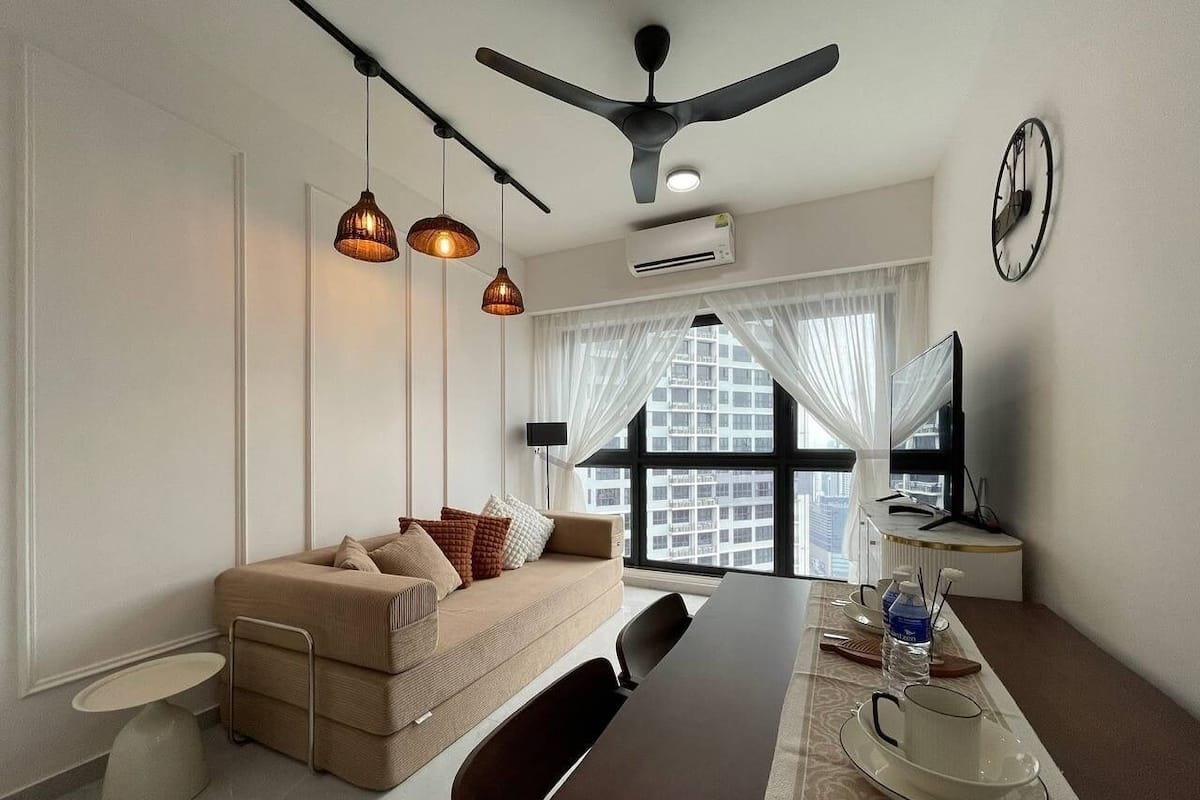 A modern hotel room with a sofa, dining table, and a large window with a city view.