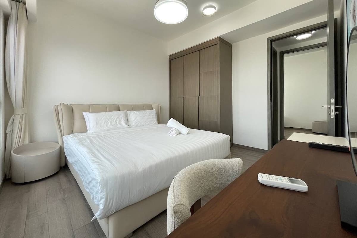 A modern hotel room with a large bed, a bedside table, a chair, a desk, and a wardrobe.