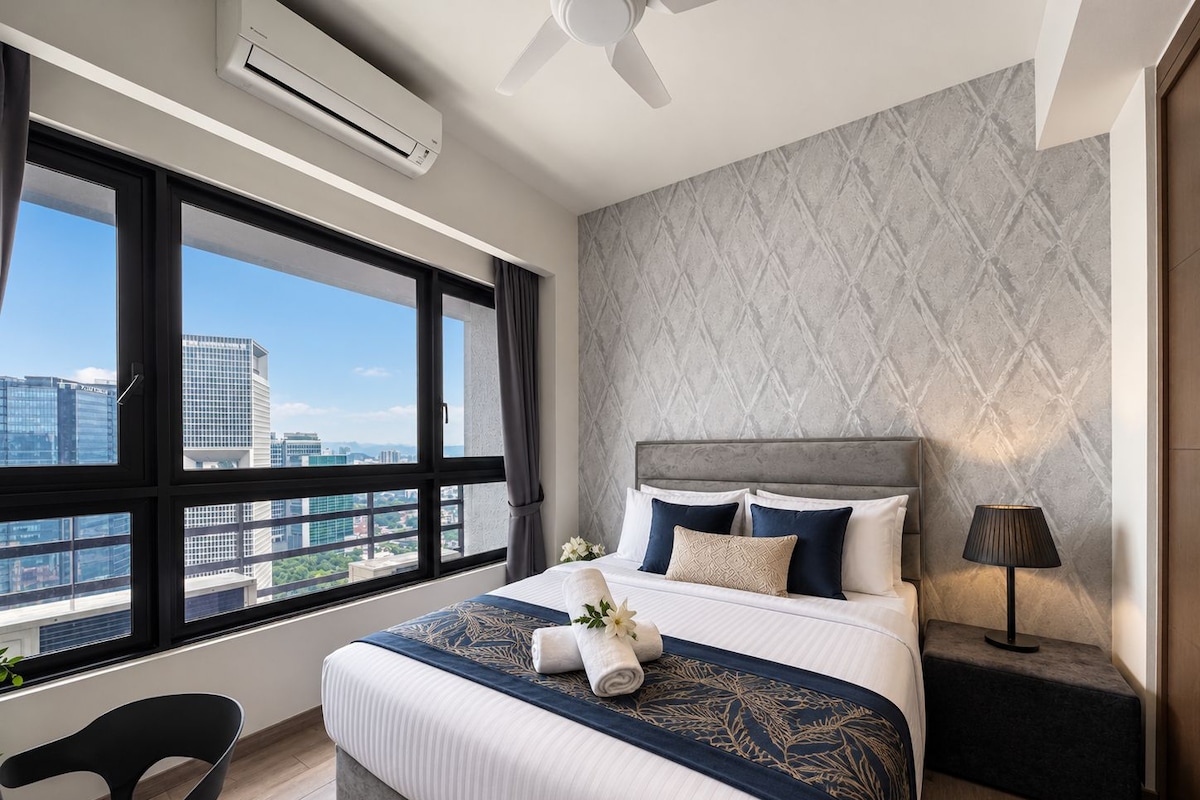 Habitación de hotel con una cama grande, vista de la ciudad a través de una ventana, un equipo de aire acondicionado y un ventilador de techo.
